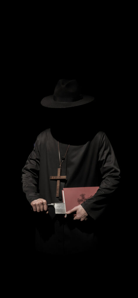 A faceless figure dressed in black holds a red book in one hand and a large knife in the other. They wear a wide-brimmed hat and a wooden cross necklace, standing against a dark background.
