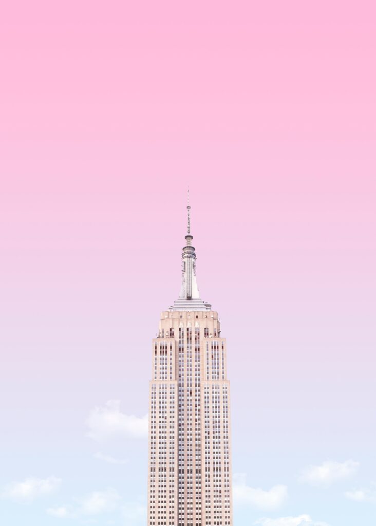 The top of a skyscraper set against a soft pink-to-blue gradient sky with a few wispy clouds, capturing a minimalist and serene atmosphere.
