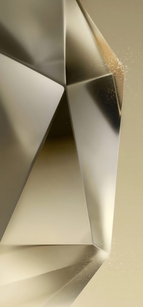 A close-up of a large, faceted, metallic sculpture with sharp edges and a reflective surface. The background is a muted gold color, complementing the sculptures sleek, geometric design, with small particles glittering near one edge.
