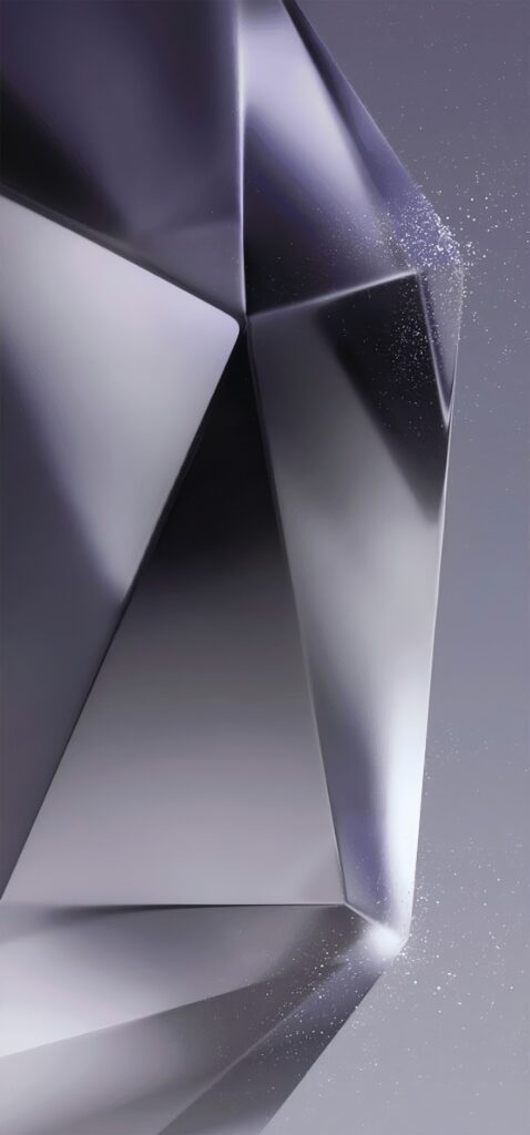 A close-up of a geometric, metallic sculpture with sharp edges and smooth surfaces. The structure reflects light, creating a sleek and modern appearance. Tiny specks around the edges add texture against a neutral background.
