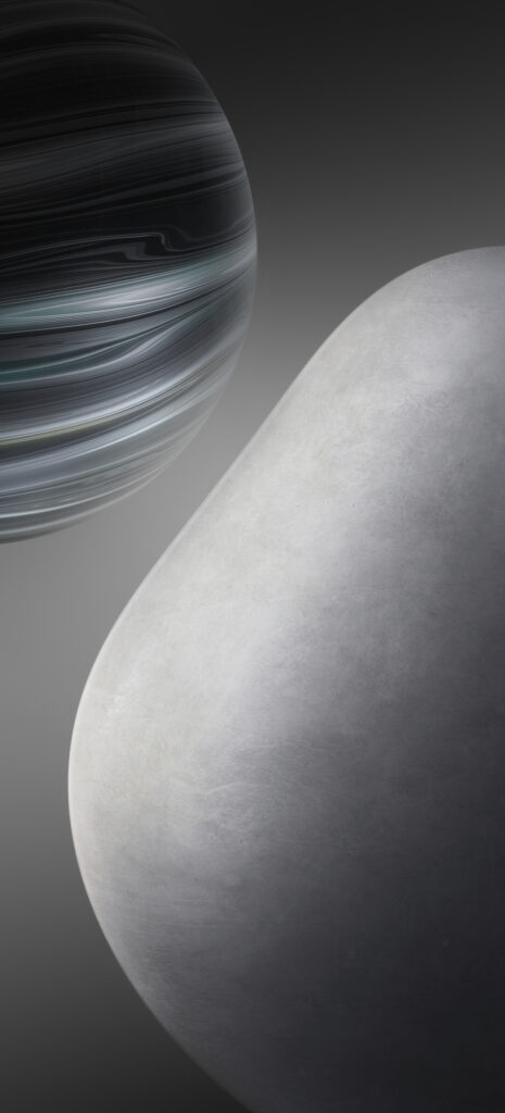 A smooth, large, gray rock sits in the foreground with a spherical, striped object resembling a planet in the background. The background is a gradient of dark gray tones.
