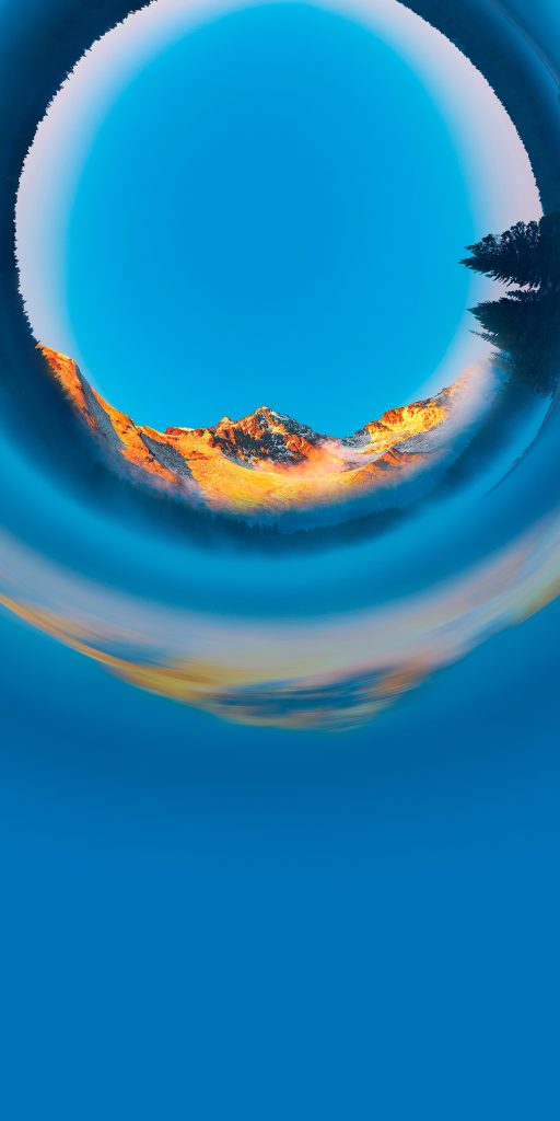 A surreal image features a glowing mountain range in warm light, bent into a circular shape against a deep blue sky. The horizon is mirrored at the base, creating a whimsical, dreamlike effect.
